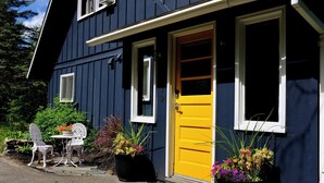 A two-story house with a yellow front door, white-framed windows, and outdoor seating with potted plants.
