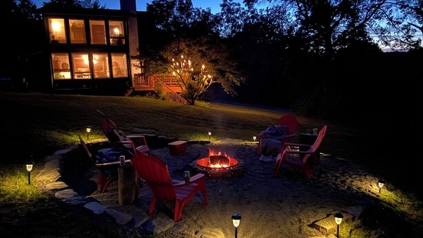 A nighttime outdoor seating area with a fire pit, red chairs, and ambient lighting.