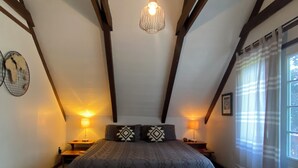 A bedroom with a large bed, two bedside tables with lamps, a chandelier, and a window with curtains.