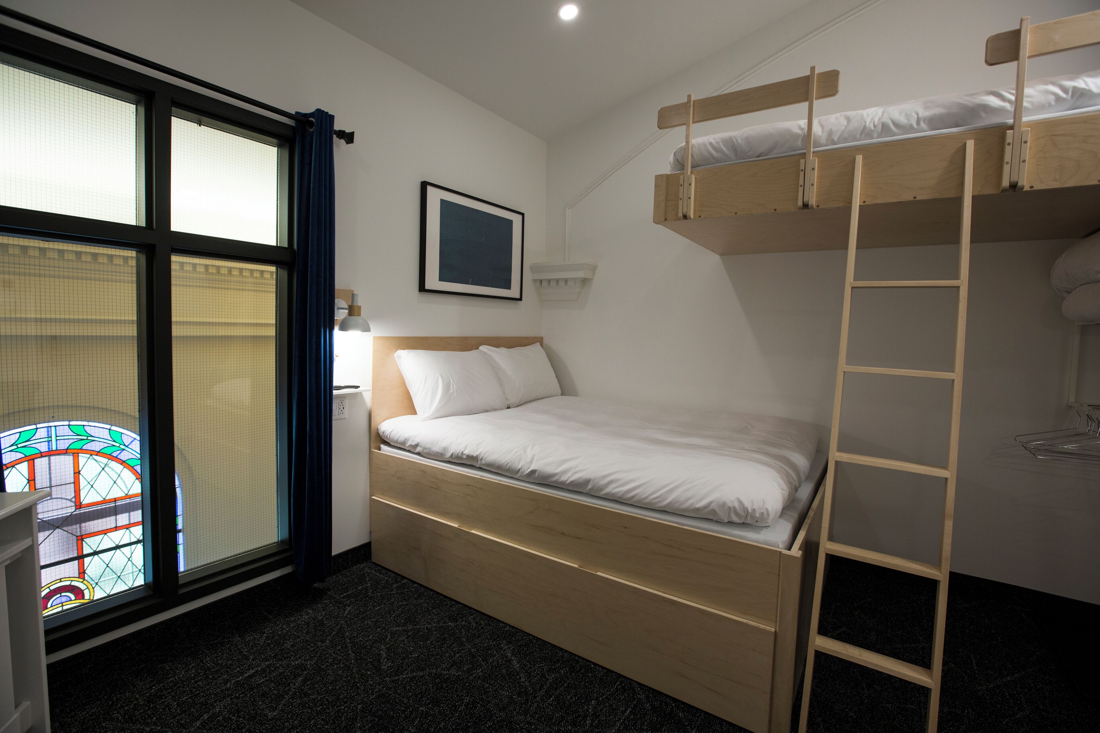 A bunk bed room with a window, a framed picture on the wall, and a ladder.