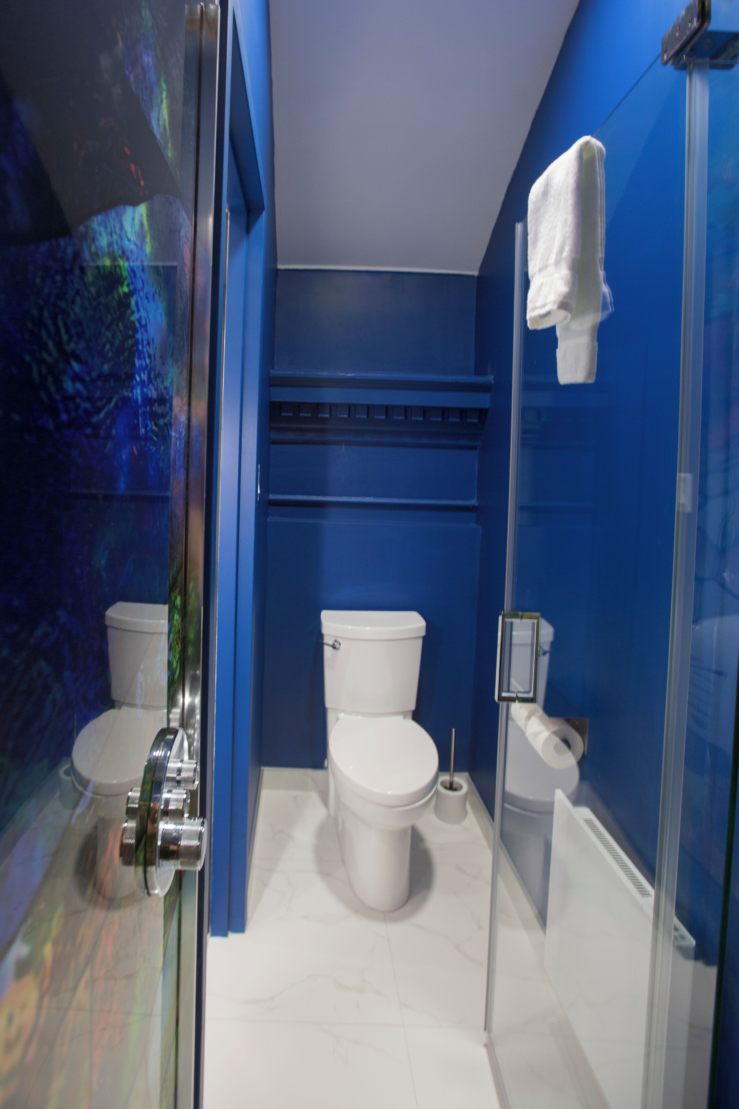 A modern bathroom with a glass shower enclosure, a white toilet, and a blue accent wall.