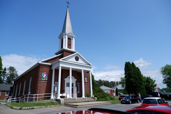 A church with a steeple, brick exterior, and a front entrance with steps. - Le Saint-Crème Alma (Alma)