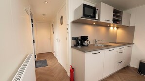 Une cuisine compacte avec des meubles blancs, un four à micro-ondes, une machine à café et un évier.