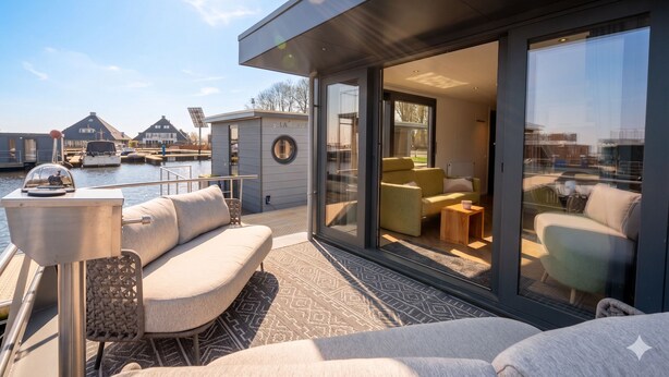 Une terrasse extérieure moderne, aménagée avec un canapé, une petite table et une porte vitrée donnant sur un espace intérieur comprenant également un canapé et une table basse.