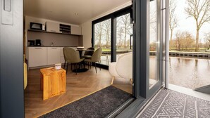 Une cuisine moderne avec un coin repas, une petite table d’appoint en bois et une vue sur un plan d’eau grâce à de grandes fenêtres.