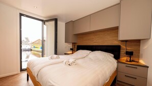 Une chambre moderne avec un grand lit, une tête de lit en bois et une porte-fenêtre coulissante donnant sur un balcon.
