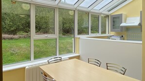 A conservatory with a table and chairs, large windows, and a view of greenery. - Cottage 466 - Clifden - sleeps 5 guests  in 3 bedrooms (Clifden)