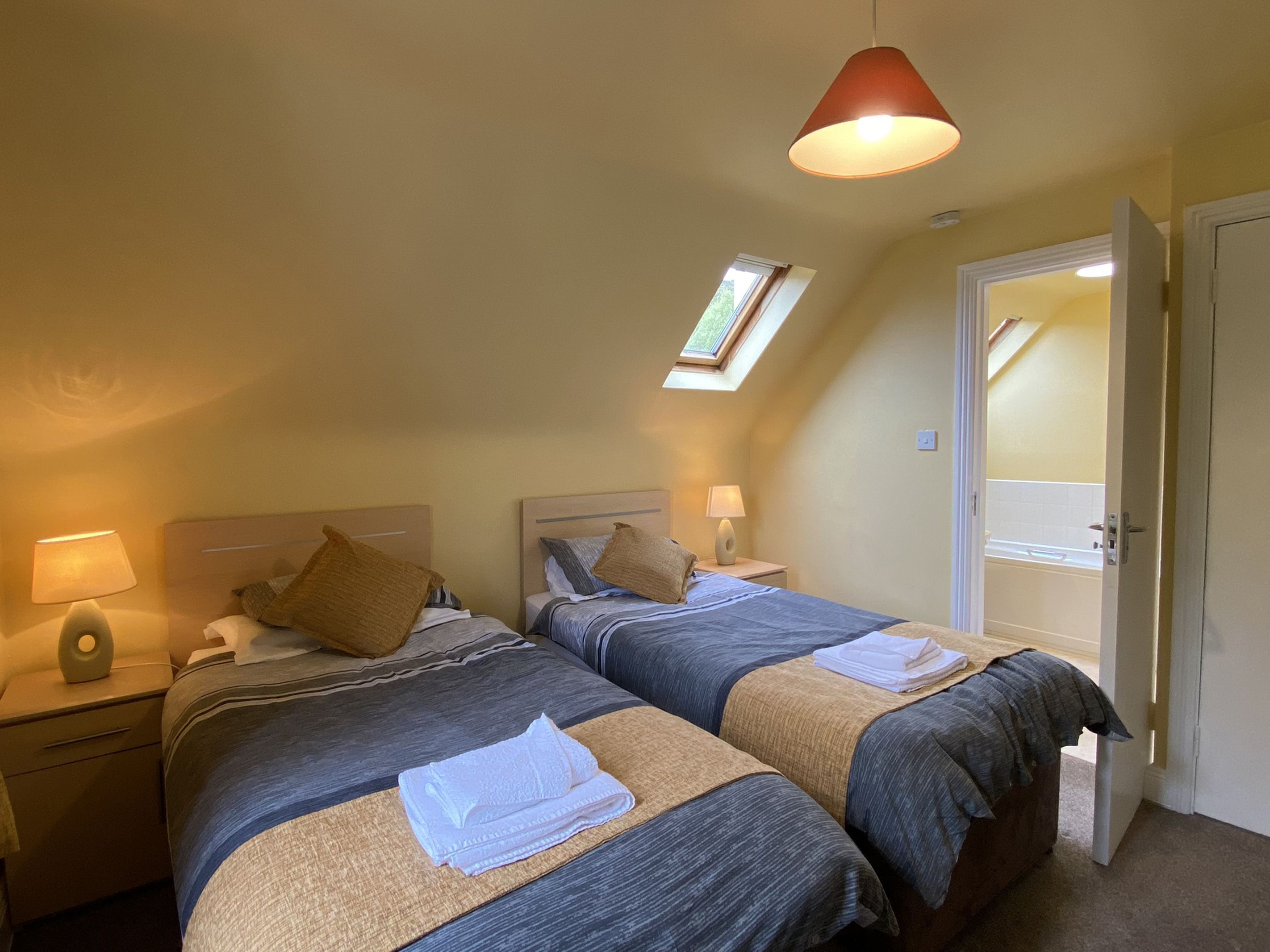 Een slaapkamer met twee bedden, een dakraam, een deur en een nachtkastje met een lamp.