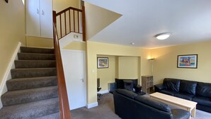 A living room with a staircase, a fireplace, a black leather sofa, and a wooden coffee table. - Cottage 466 - Clifden - sleeps 5 guests  in 3 bedrooms (Clifden)