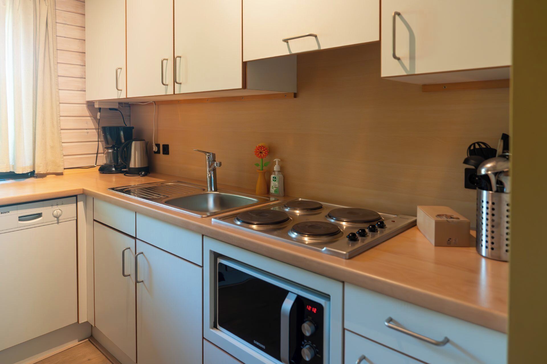 Eine moderne Küche mit weißen Schränken, einem Geschirrspüler von Bosch, einem Samsung-Backofen und einem Edelstahlkochfeld.