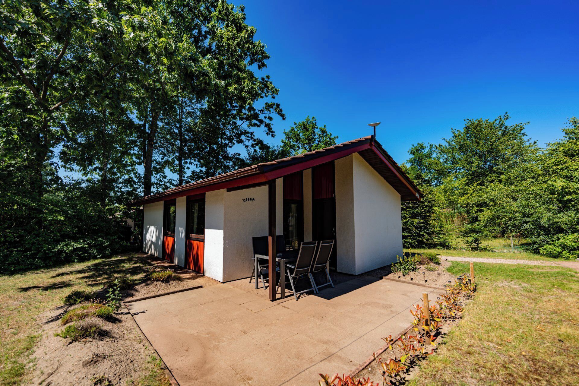 Een laag, enkelstaand gebouw met een rood dak en witte muren, met een terras en twee stoelen en een tafel.