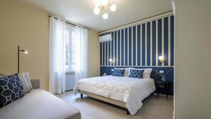 Een slaapkamer met een bed, een bank, een raam met gordijnen, een radiator en een aan de muur bevestigde airconditioner.