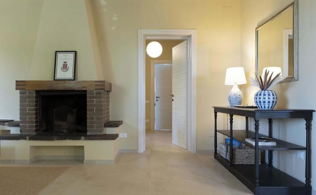 Een gang met een open haard, een console tafel met een lamp, en een spiegel aan de muur.