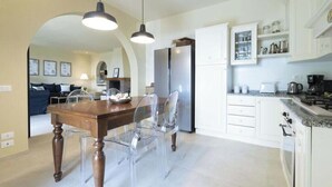 Een moderne keuken met witte kasten, een roestvrijstalen koelkast en een eethoek met een houten tafel en transparante stoelen.