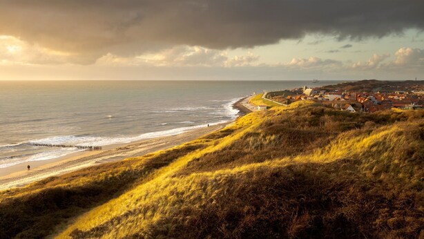 Eine Küstenstadt mit Strand, grünen Hügeln und einem stürmischen Himmel.