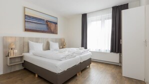 Ein modernes Hotelzimmer mit einem großen Bett, einem Nachttisch mit Lampen, einem Bild an der Wand und einem Fenster mit Vorhängen.
