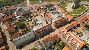 Eine Vogelperspektive einer Küstenstadt mit traditionellen Gebäuden mit roten Dächern, einer Kirche und einem Strand im Hintergrund.