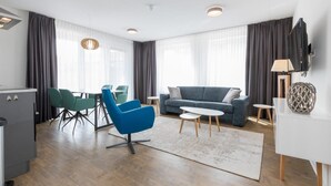 Ein modernes Wohnzimmer mit Sofa, Sesseln, Couchtisch und einem Essbereich mit Tisch und Stühlen.