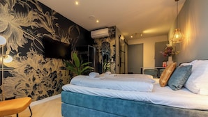 A modern bedroom with a large bed, a flat-screen TV mounted on the wall, and a ceiling-mounted air conditioning unit. - Studio - Van der Manderelaan 16 'Studio B' | Koudekerke (Koudekerke)