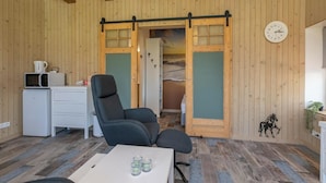 Una habitación con paredes de madera, un escritorio blanco, una silla de oficina negra, una pequeña mesa con vasos y un reloj en la pared.