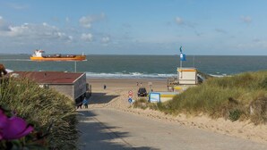 Una playa con un sendero arenoso que lleva al mar, una torre de salvavidas y un barco grande a lo lejos.