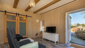 Una habitación con paredes de madera, una puerta corredera, un televisor sobre un aparador blanco, un reloj y vistas al exterior.