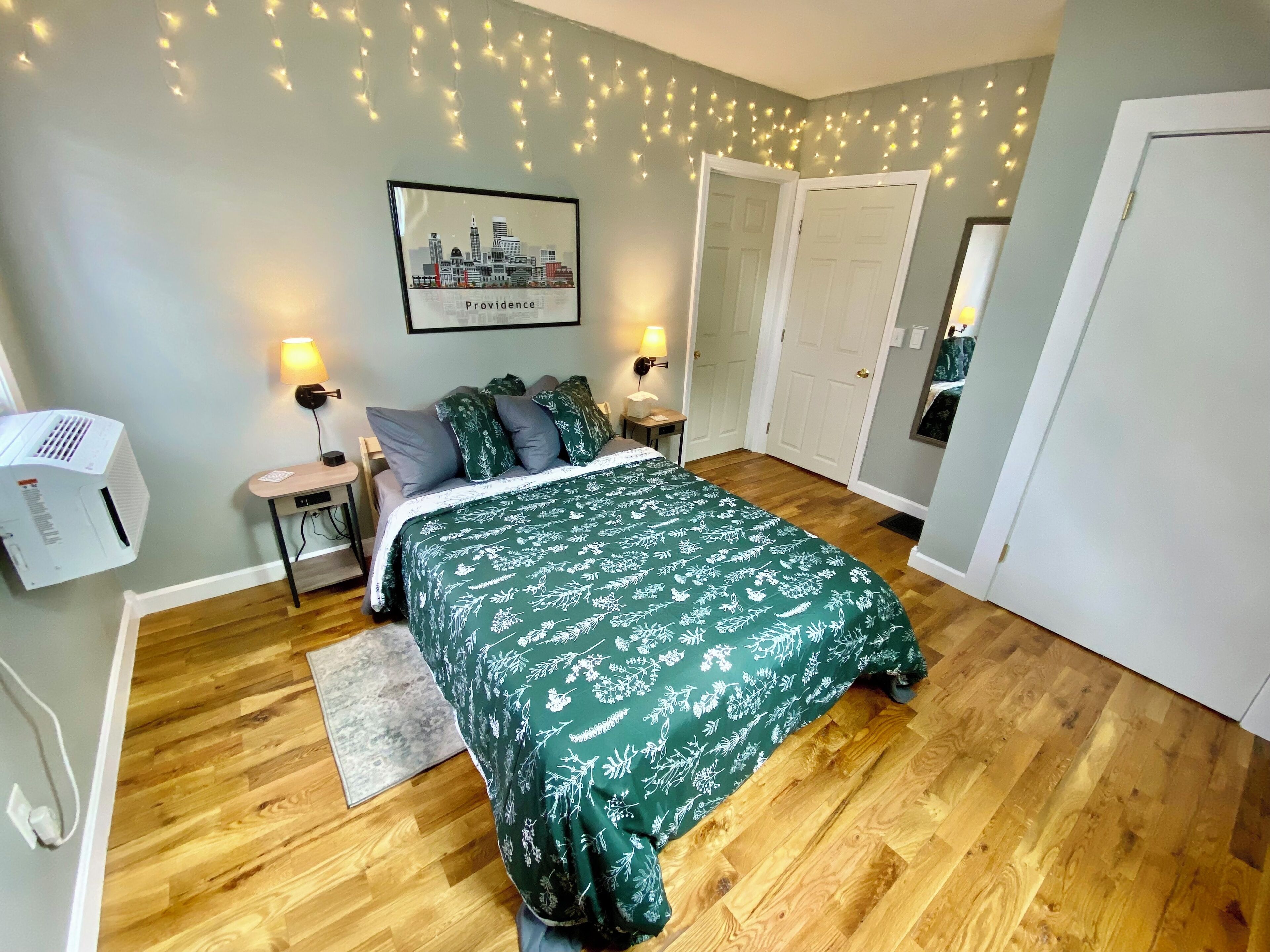 Een slaapkamer met een bed, nachtlampjes, een stadsgezicht in een lijst, een verwarming en een deur.