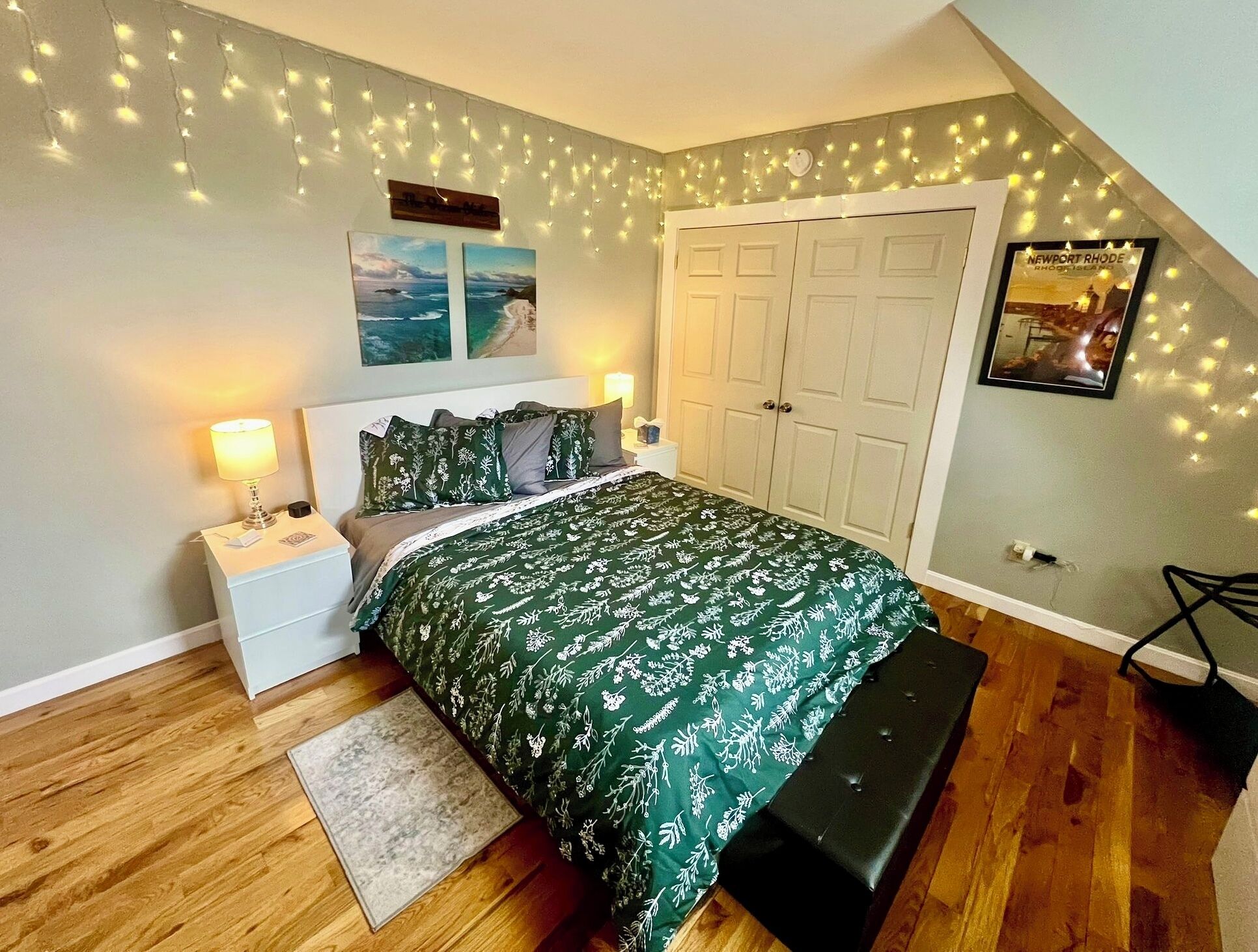 Ein Schlafzimmer mit Bett, Nachttischen, einer Bank, einer Tür und Lichterketten.
