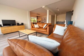 Relax in this stylish living room with a large leather sofa, dining area, and modern kitchen.