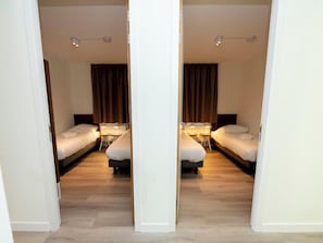 Two single beds with bedside tables and lamps, set against a mirrored wall.
