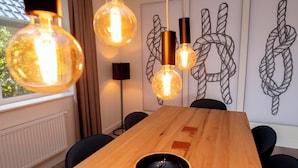 Une salle de conférence avec une table en bois, des chaises noires et des luminaires suspendus dotés d’ampoules apparentes.