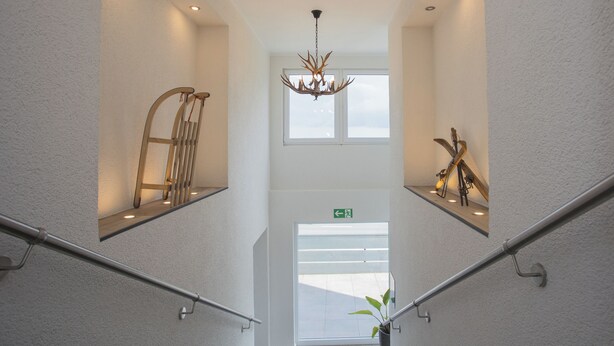 Un escalier moderne avec des rampes en métal, un lustre et une plante à sa base.