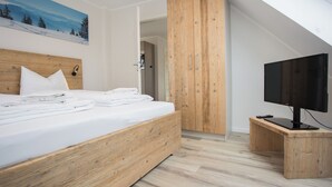 Une chambre à coucher moderne avec un lit en bois, un téléviseur posé sur un meuble en bois et un tableau accroché au mur.