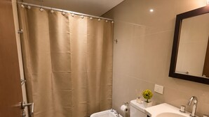 A modern bathroom with a shower curtain, a bidet, a toilet, and a sink with a mirror. - GURRUCHAGA PALERMO (Buenos Aires)