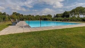 Ein rechteckiger Pool mit Fliesen umgeben, umgeben von Gras und Bäumen.