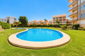 A swimming pool surrounded by well-maintained grass, with a clear blue sky above.