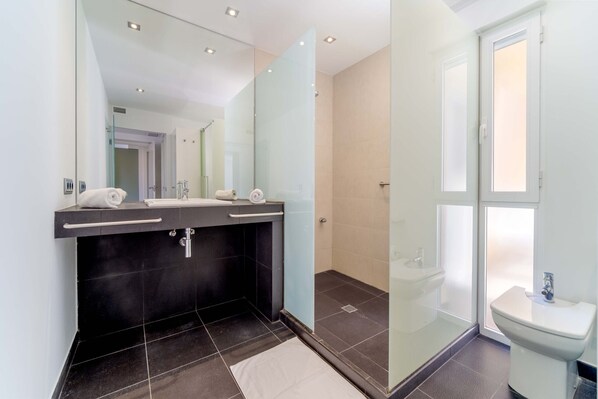 Une salle de bain moderne avec un sol carrelé foncé, une douche en verre et un lavabo blanc.