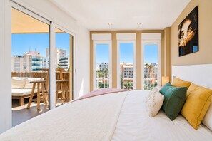 Une chambre d’hôtel avec un grand lit, un balcon donnant sur la ville et un tableau accroché au mur.