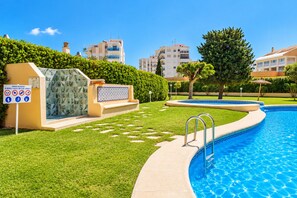 Une piscine avec une terrasse carrelée, un panneau indiquant les heures d’ouverture et une pelouse bien entretenue.