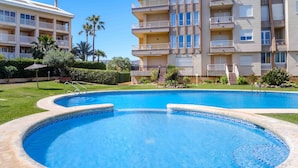 Una piscina con diseño curvo, rodeada de un césped cuidado y un edificio de varios pisos con balcones.