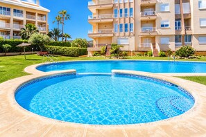 Une piscine dont le bord est recouvert de carrelage, entourée d’une pelouse bien entretenue et de palmiers.