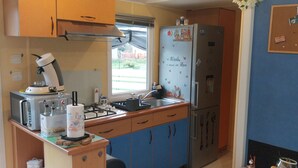 A compact kitchen with a gas stove, a microwave, a refrigerator, and a window providing a view of the outdoors. - Mobile homes in the countryside  (Saint-Loup)
