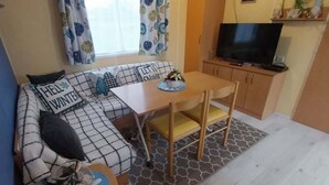 A compact living space with a sofa, a small dining table, a TV, and a kitchenette. - Mobile homes in the countryside  (Saint-Loup)