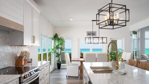 A spacious kitchen with a large island, white cabinetry, and a view of the ocean. - Beachfront Luxury Estate Sleeps 20 & Allows Events (Navarre)