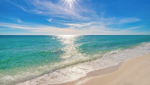 A beach with clear turquoise water, gentle waves, and a bright sun shining over the horizon. - Beachfront Luxury Estate Sleeps 20 & Allows Events (Navarre)