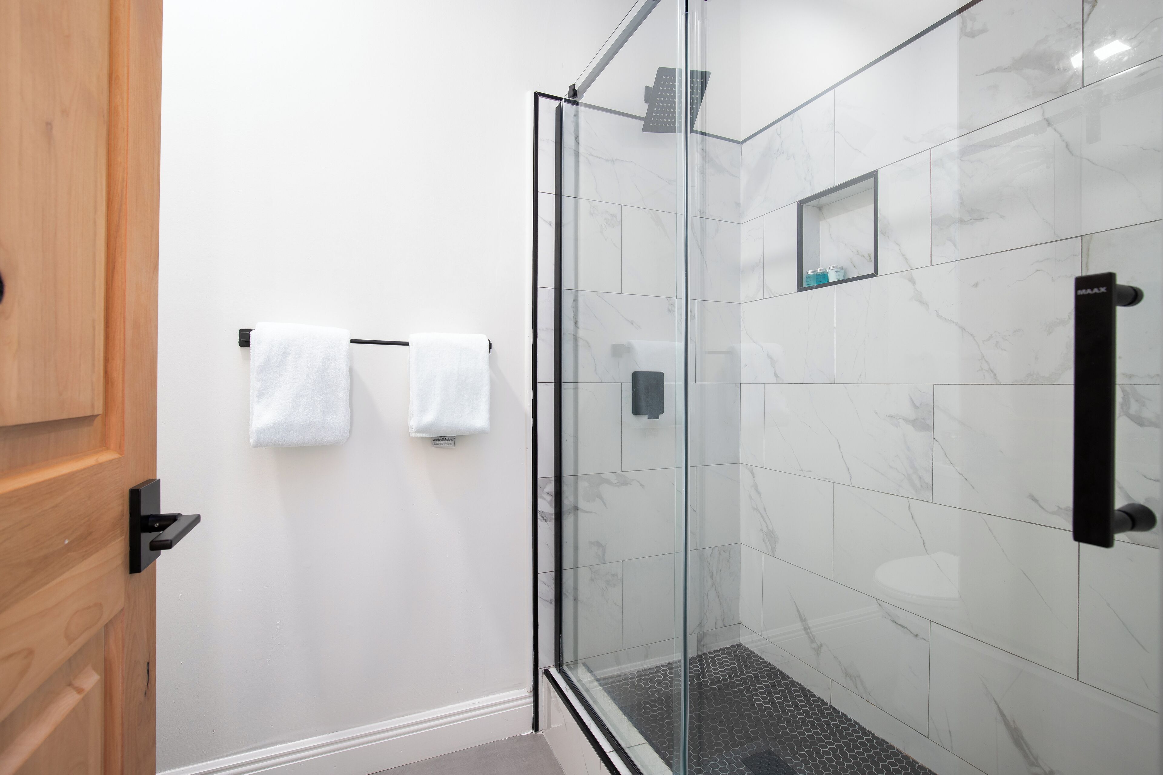 Une salle de bain moderne avec une douche à parois de verre, des carreaux de marbre blanc et une porte en bois.