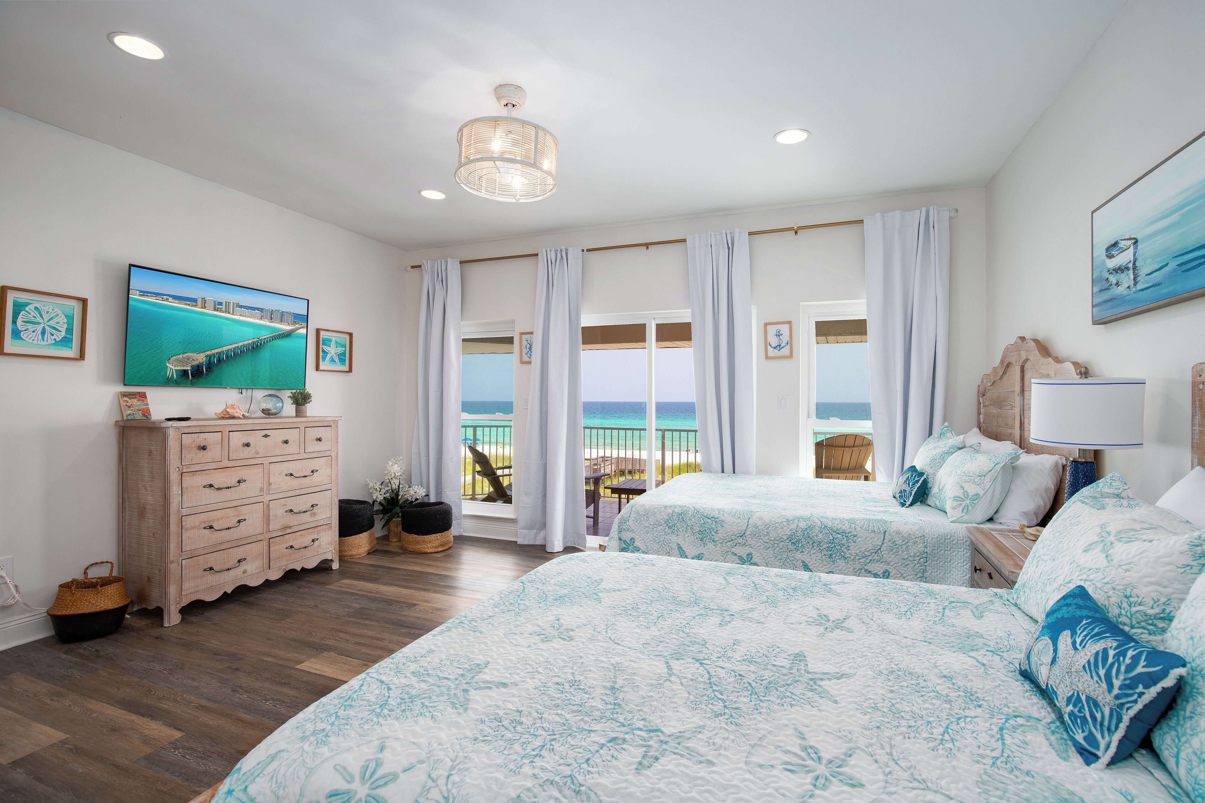 A bedroom with two beds, a television, a wooden dresser, and a view of the beach.