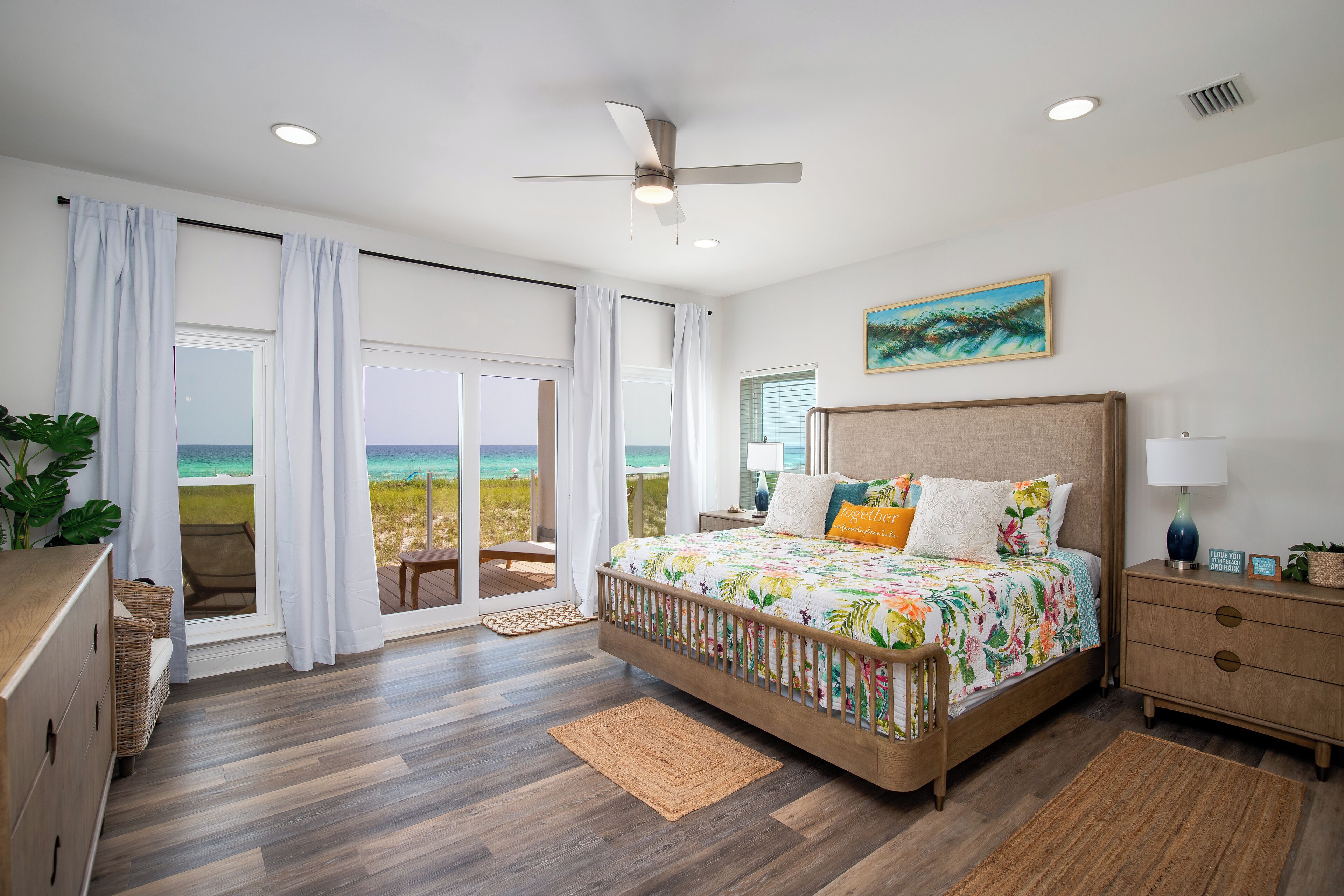A bedroom with a large bed, a ceiling fan, and a view of the beach.