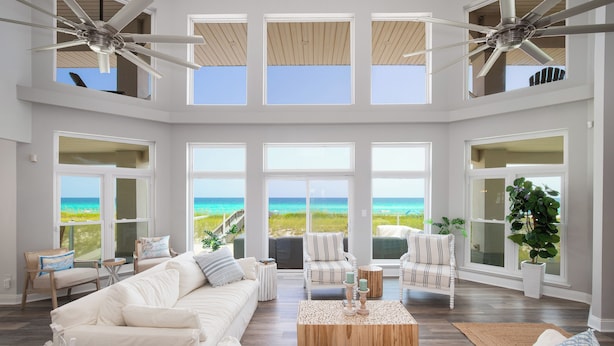 A spacious living room with a large white sofa, striped chairs, and a wooden coffee table. Large windows offer views of the ocean. - Beachfront Luxury Estate Sleeps 20 & Allows Events (Navarre)