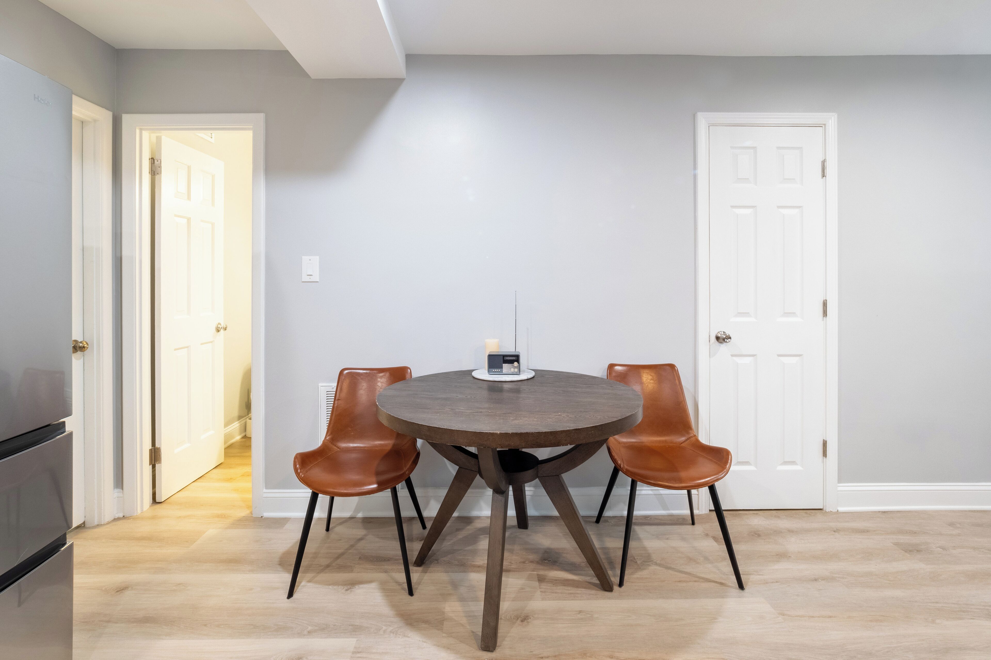 Un coin repas avec une table ronde, deux chaises marron et une porte blanche en arrière-plan.
